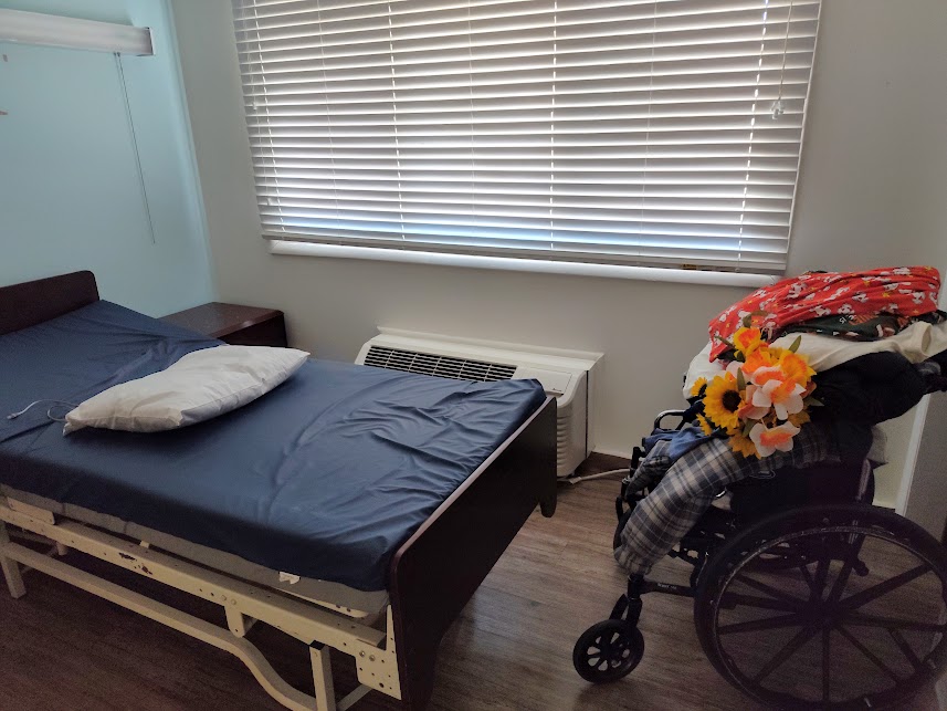 empty and stripped bed with belongings in wheelchair beside it